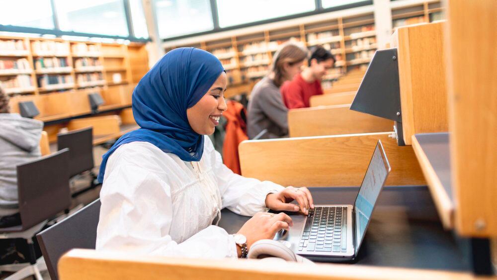 Person jobber på laptop på lesesal i et bibliotek