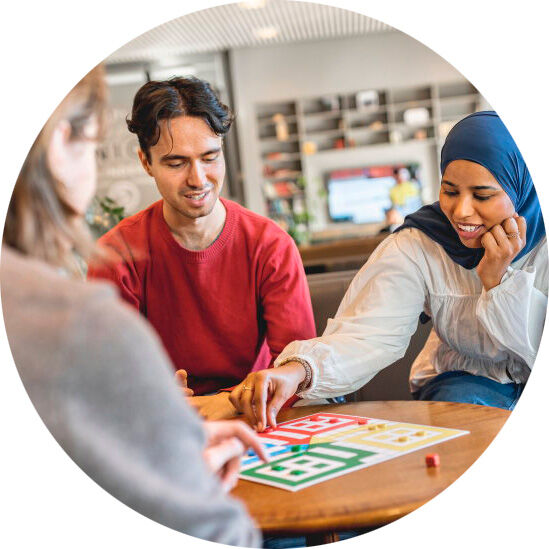 Tre personer sitter rundt et bord og spiller ludo