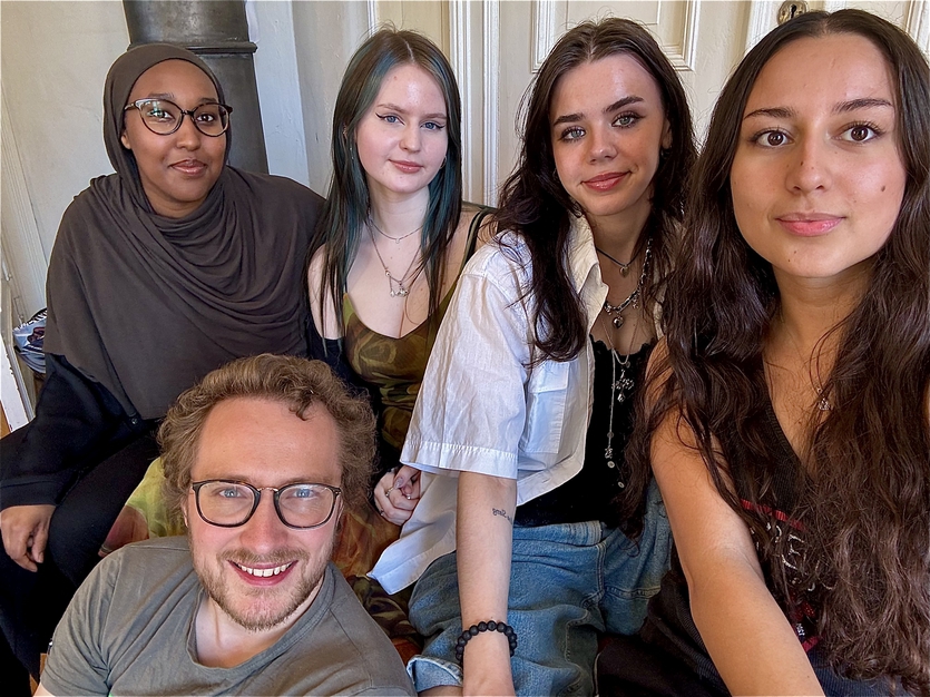 Gruppe bilded av alle 5 medlemmer. Sitter i en sofa, og poserer emd smil til bildet.