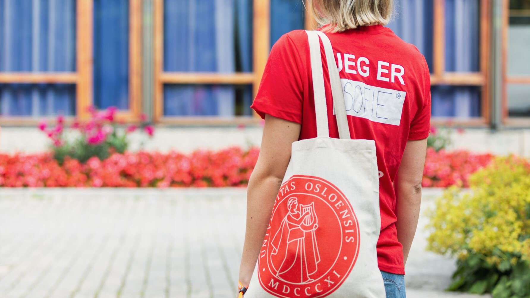 Fadder med rød tskjorte og handlenett med UiO-logo på campus i studiestart.