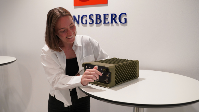 Ung dame med mellomkort brunt hår og hvit skjorte skurr på en radio fra forsvaret som heter Thor.
