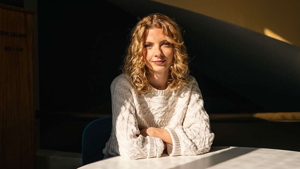 Portrett av Leah sittende ved et rundt bord; blonde krøller; hvit genser