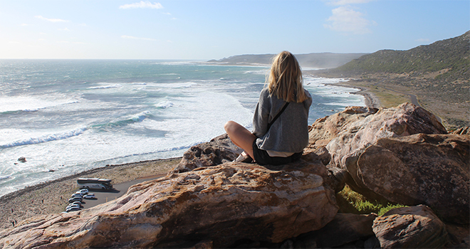 Jente sitter på klippe og ser utover havet i Sør-Afrika