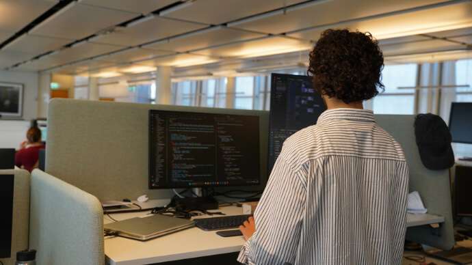 Ung mann med brunt krøllete hår står ved pc-en sin.