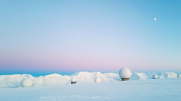Landskap i snø med KSAT sin bakkestasjon på Svalbard