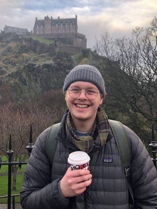 smilende person med kaffekopp lue og vinterjakke
