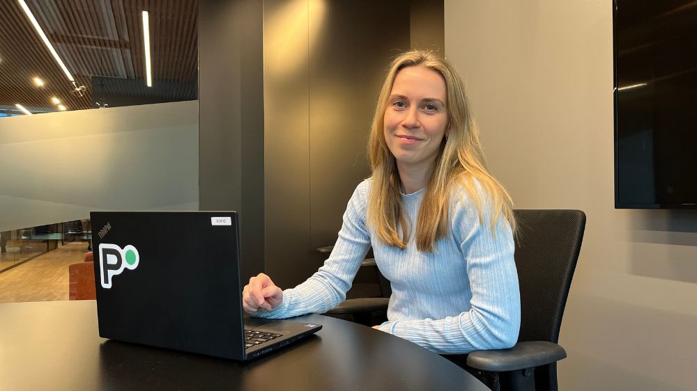 Blond jente i lyseblå genser sitter foran PC´en på kontoret. 