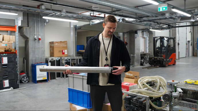 En ung mann med brunt hår står i kjelleren i NGIs lokaler og viser frem utstyr som brukes til å kartlegge kvikkleire og risikoen for kvikkleireskred.