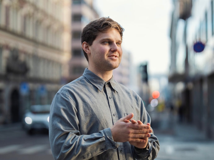 Jakob ute i gate, gestikulerer, grå skjorte, smiler.