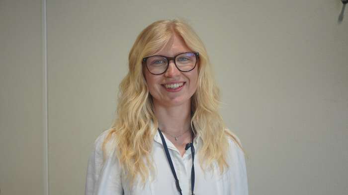 Ung dame med blondt hår og briller smiler til kamera. 