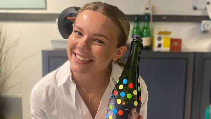 Ung dame som smiler i labfrakk og som holder en dekorert falske. 