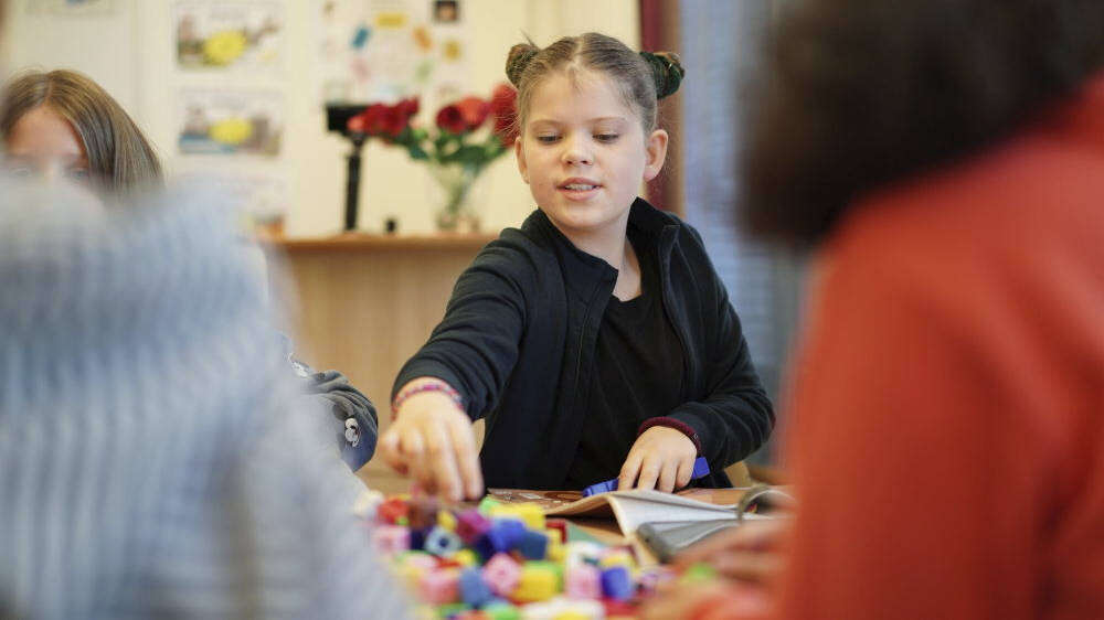 Et jentebarn sitter og løser oppgaver med fargerike klosser foran seg, konsentrert mens hun utforsker formene.