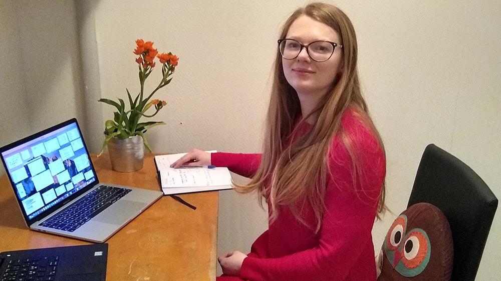 Solveig sitter ved sitt skrivebord på hjemmekontoret, med kaffeekopp, to skjermer og en blomst