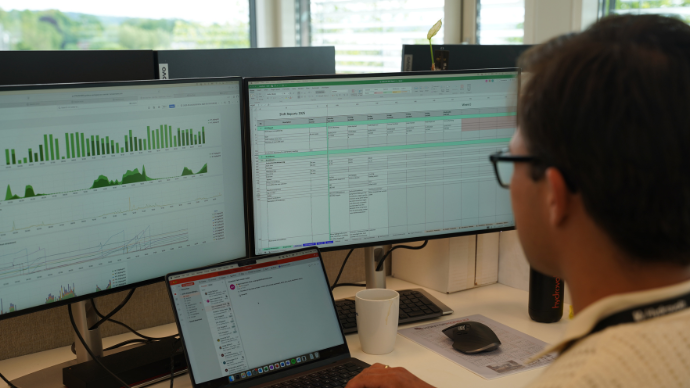 Bilde av en ung mann bakfra som sitter og jobber foran en pc-skjerm med forskjellig statstikk. 