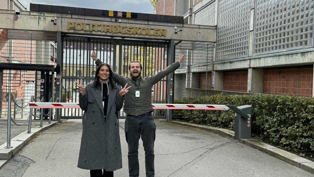 Studentene Joel og Rajki poserer foran porten til Politihøyskolen