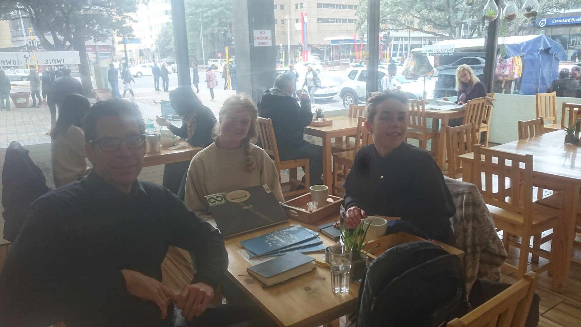 Tre personer som sitter rundt et bord på en kafe. To kvinner og en mann. 