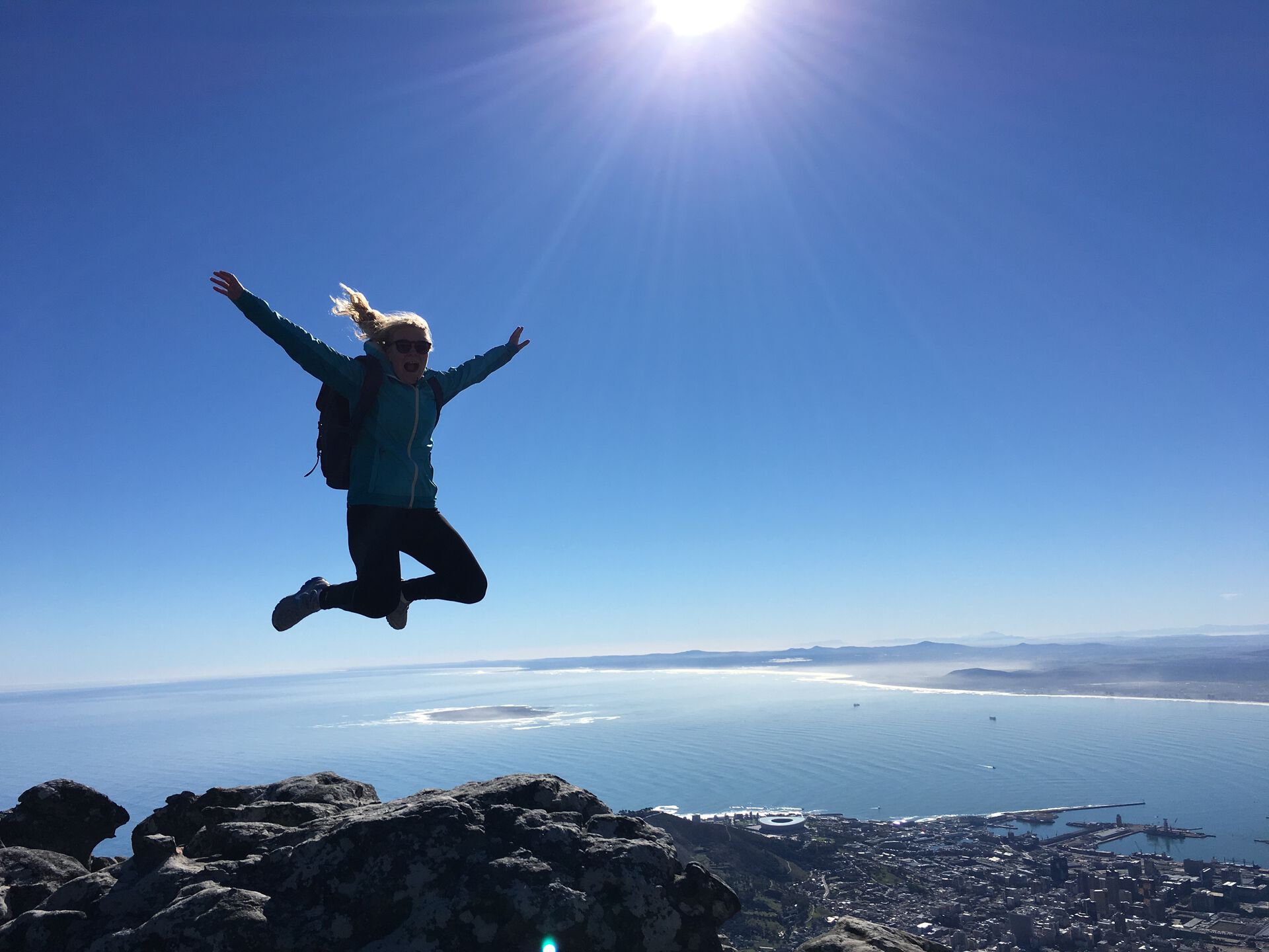 Jente som hopper på toppen av et fjell med byen Cape Town i bakgrunnen