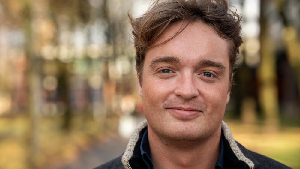 Mann som smiler, uklar bakgrunn, ute på campus