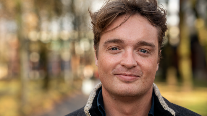 Mann som smiler, uklar bakgrunn, ute på campus