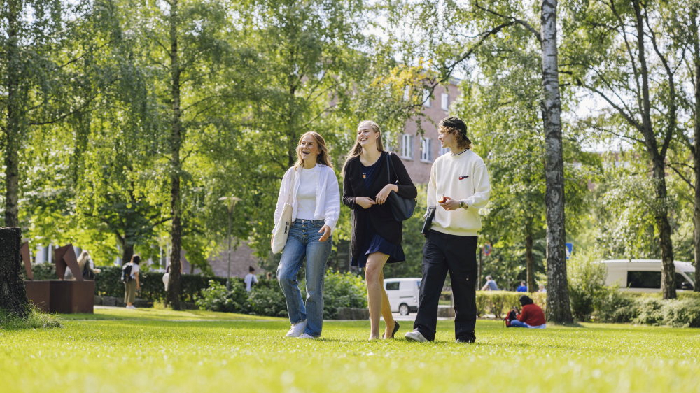 Tre studenter går over universitetshage på sommeren.