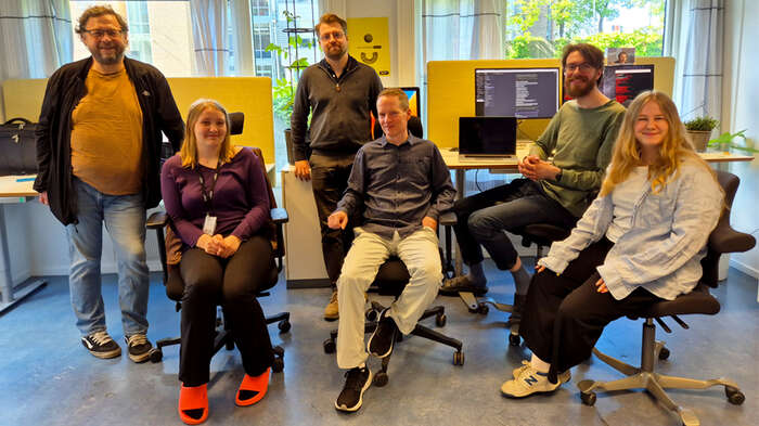 Photo of six happy developers in an open-plan office.