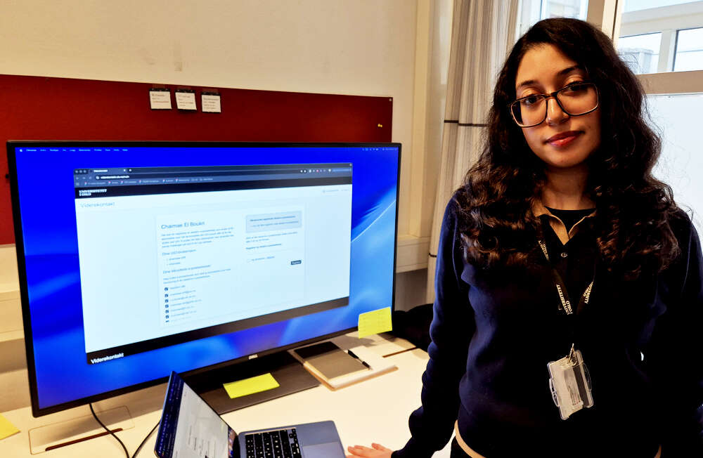 Young woman with long dark hair and glasses in front of a computer screen displaying the front page of the Viderekontakt IT service.