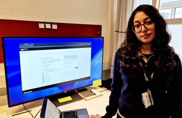 Young woman with long dark hair and glasses in front of a computer screen displaying the front page of the Viderekontakt IT service.
