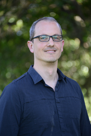 Dale Barr smiling, glasses, blue shirt, nature background
